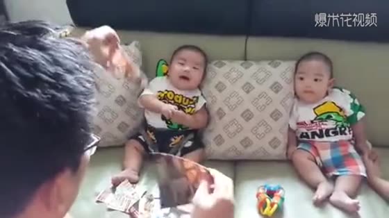 Dad tears paper to amuse the twins. The reaction of the two children is too different.