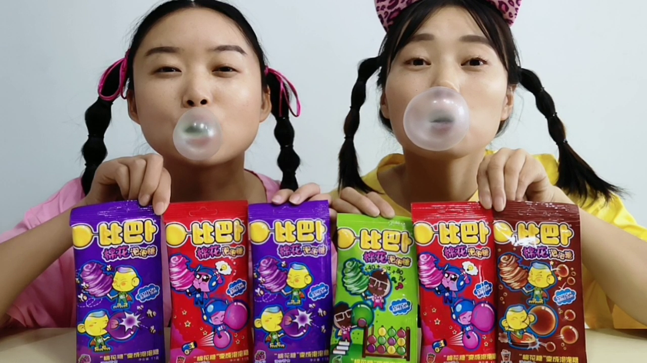 Two girlfriends eat "cotton bubble gum", which is bigger than who blows big, and slap hard on their faces is super funny.