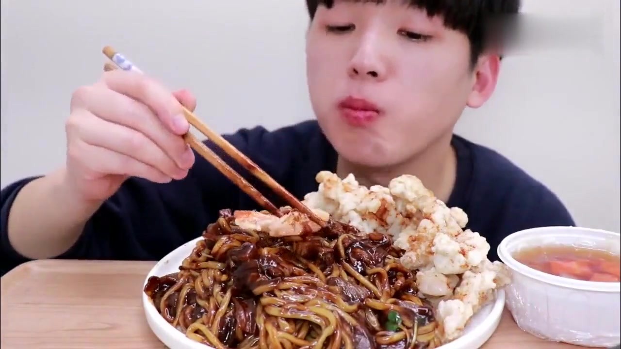 The handsome boy eats fried sauce noodles and fried crispy meat. He eats the whole course without talking. He chews and listens to greedy people.